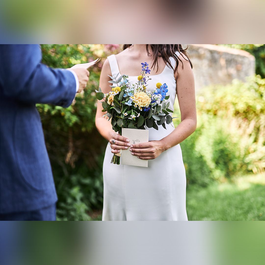 Mariée tenant son bouquet et une lettre dans un jardin, pendant un moment intime avant la cérémonie