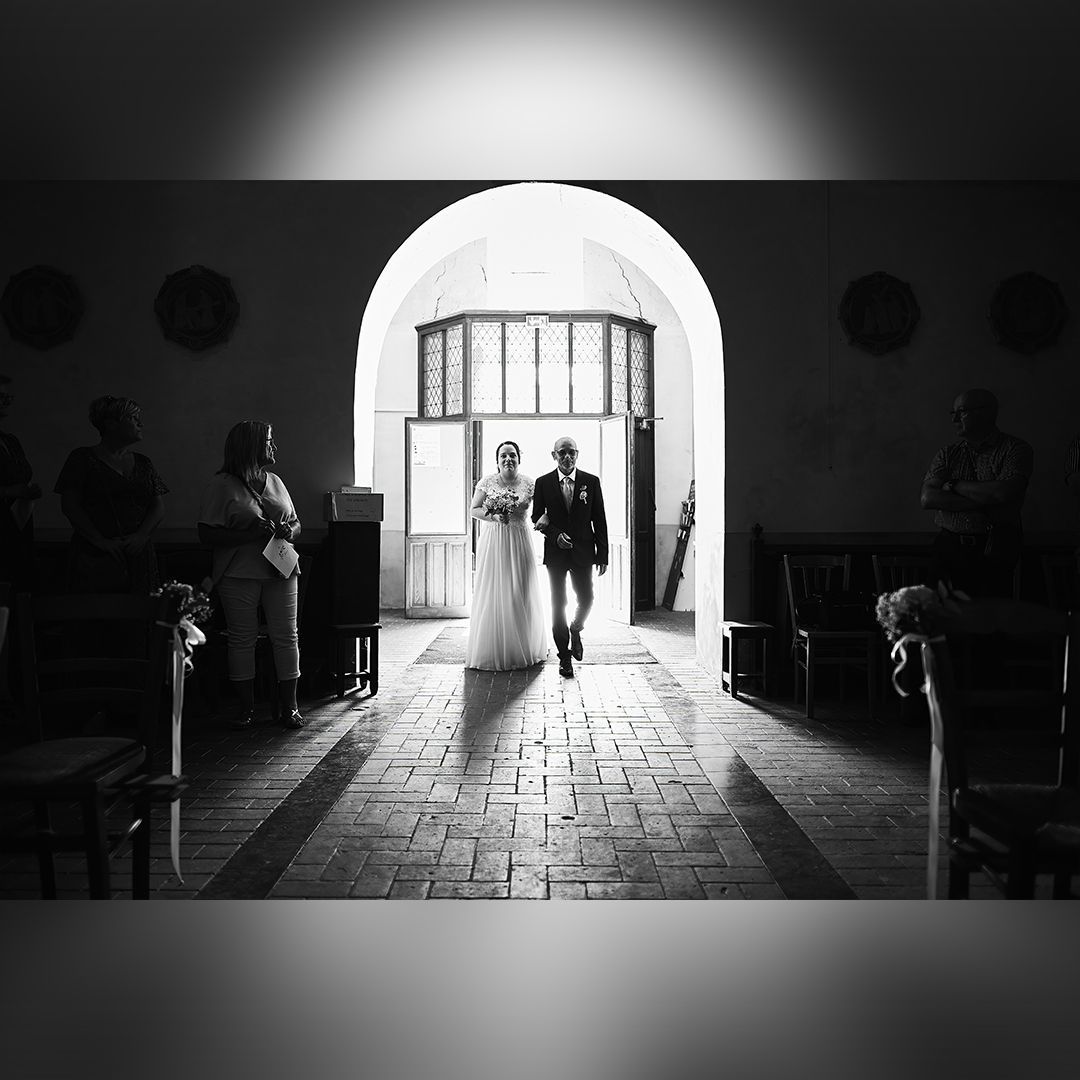 Mariée entrant dans une église accompagnée d’un proche, sous le regard des invités