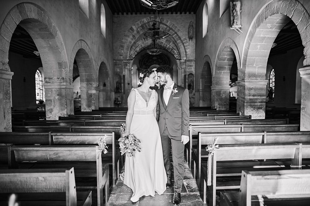 Julie et Guilhem posent dans l’allée d’une église après la cérémonie