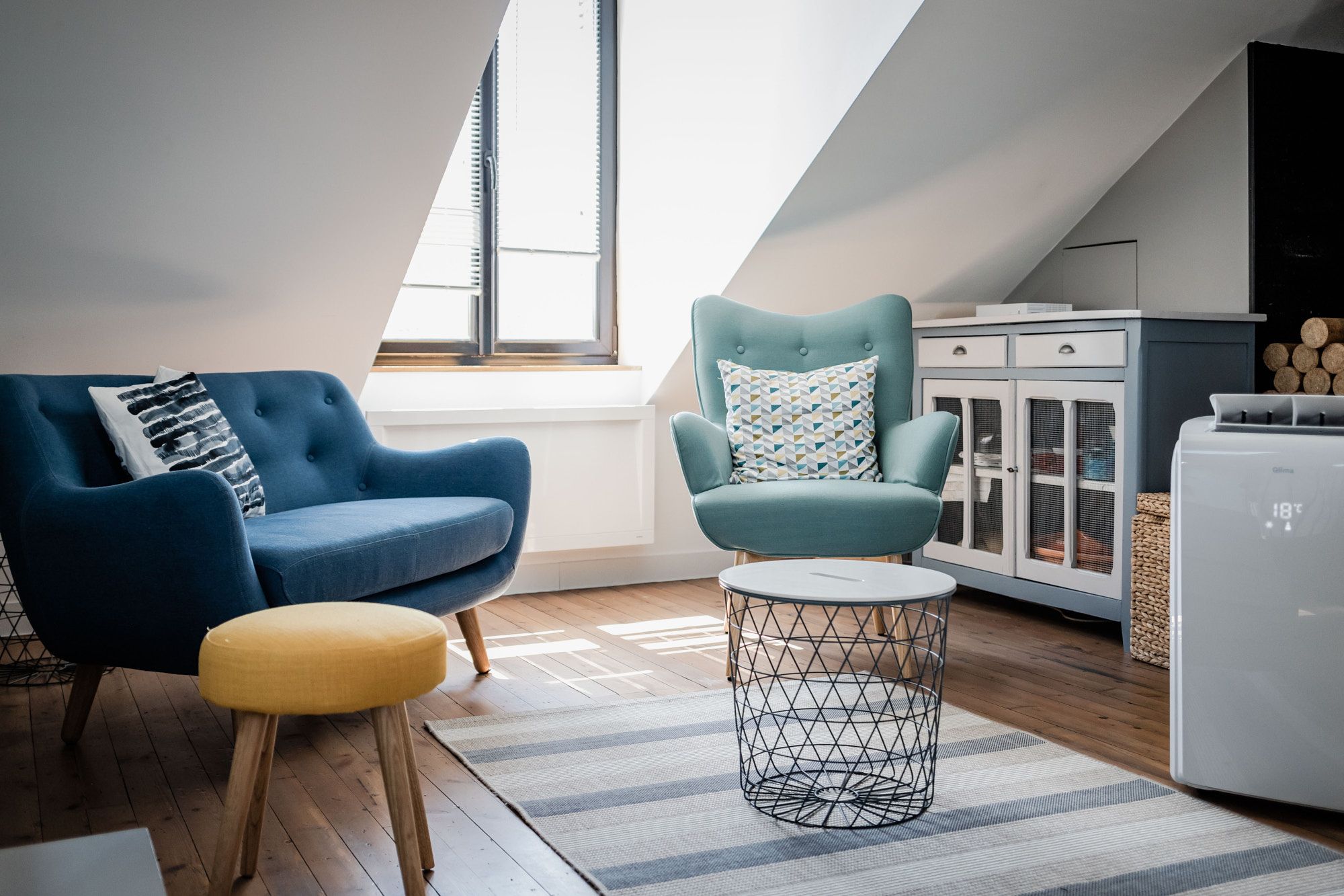 Salon mansardé lumineux avec fauteuils bleus, table basse et meuble bas