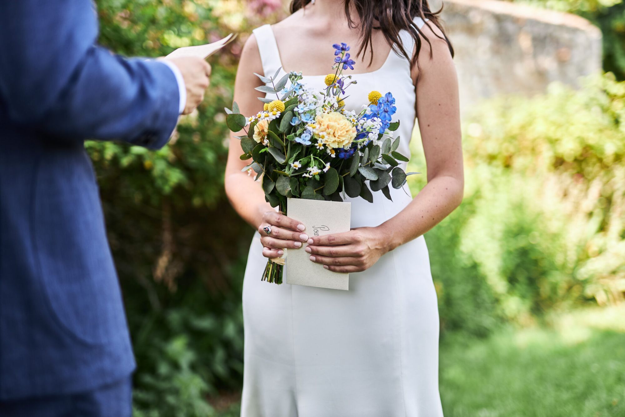 Mariée tenant son bouquet et une lettre dans un jardin, avec son mari à ses côtés